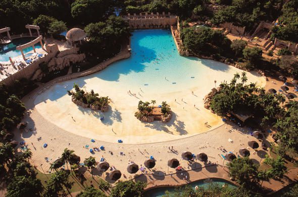 An aerial view of the Valley of Waves water park at Sun City Resort, showcasing the sandy beach and wave pool as a top leisure attraction for visitors and families.